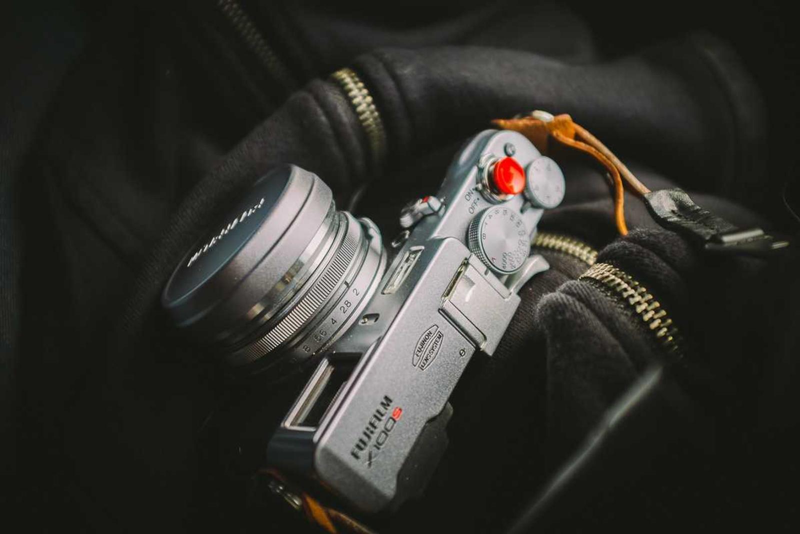 A silver compact camera with a red shutter button resting in the open pocket of a black bag